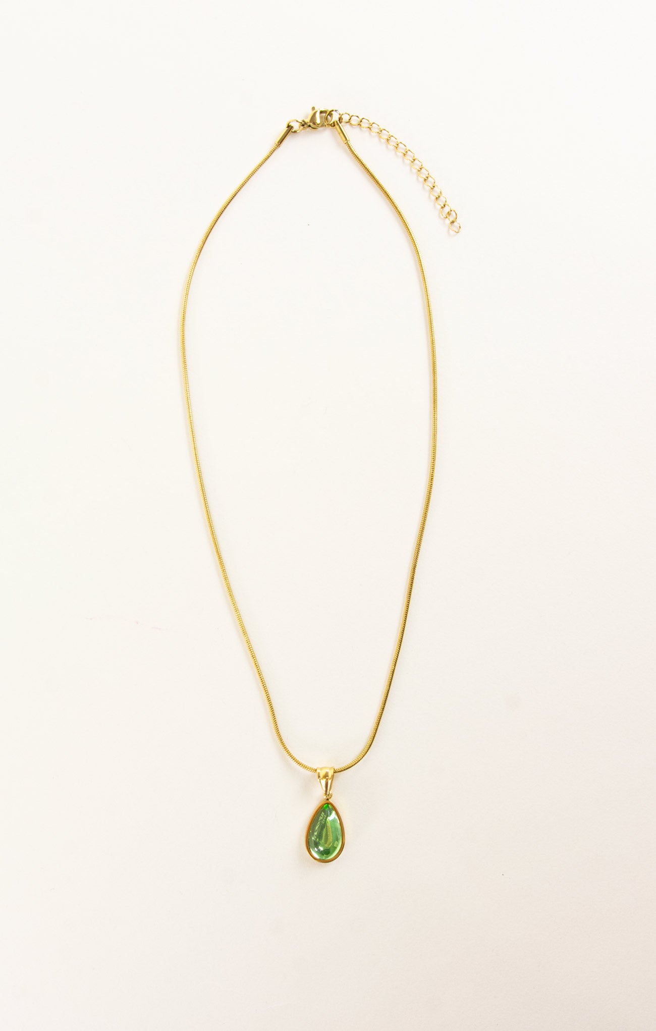 Gold necklace with a green teardrop pendant on a beige background