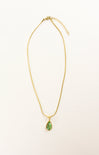 Gold necklace with a green teardrop pendant on a beige background