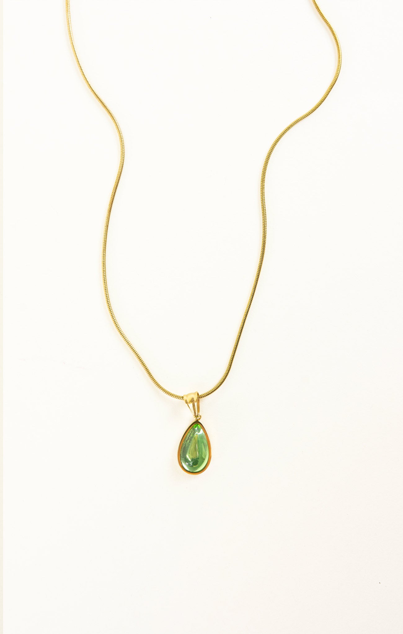 Gold necklace with a green teardrop pendant on a white background