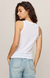Woman wearing a white sleeveless top and light blue jeans against a beige background