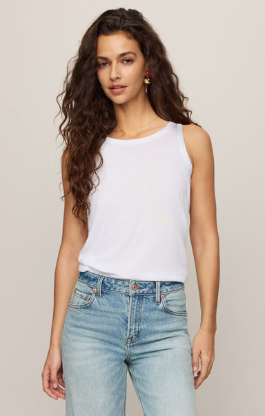Woman wearing a white tank top and light blue jeans against a plain background