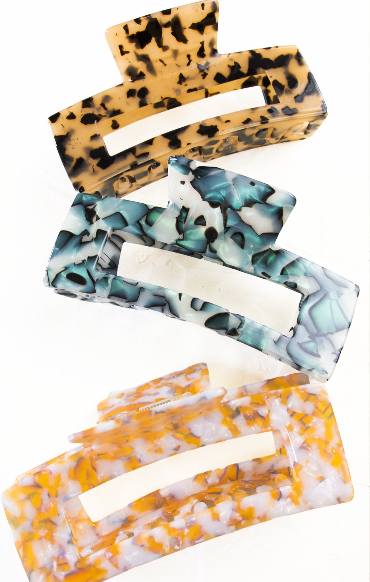 Set of three hair clips with leopard print, blue and white marble, and orange and white pattern on a white background.