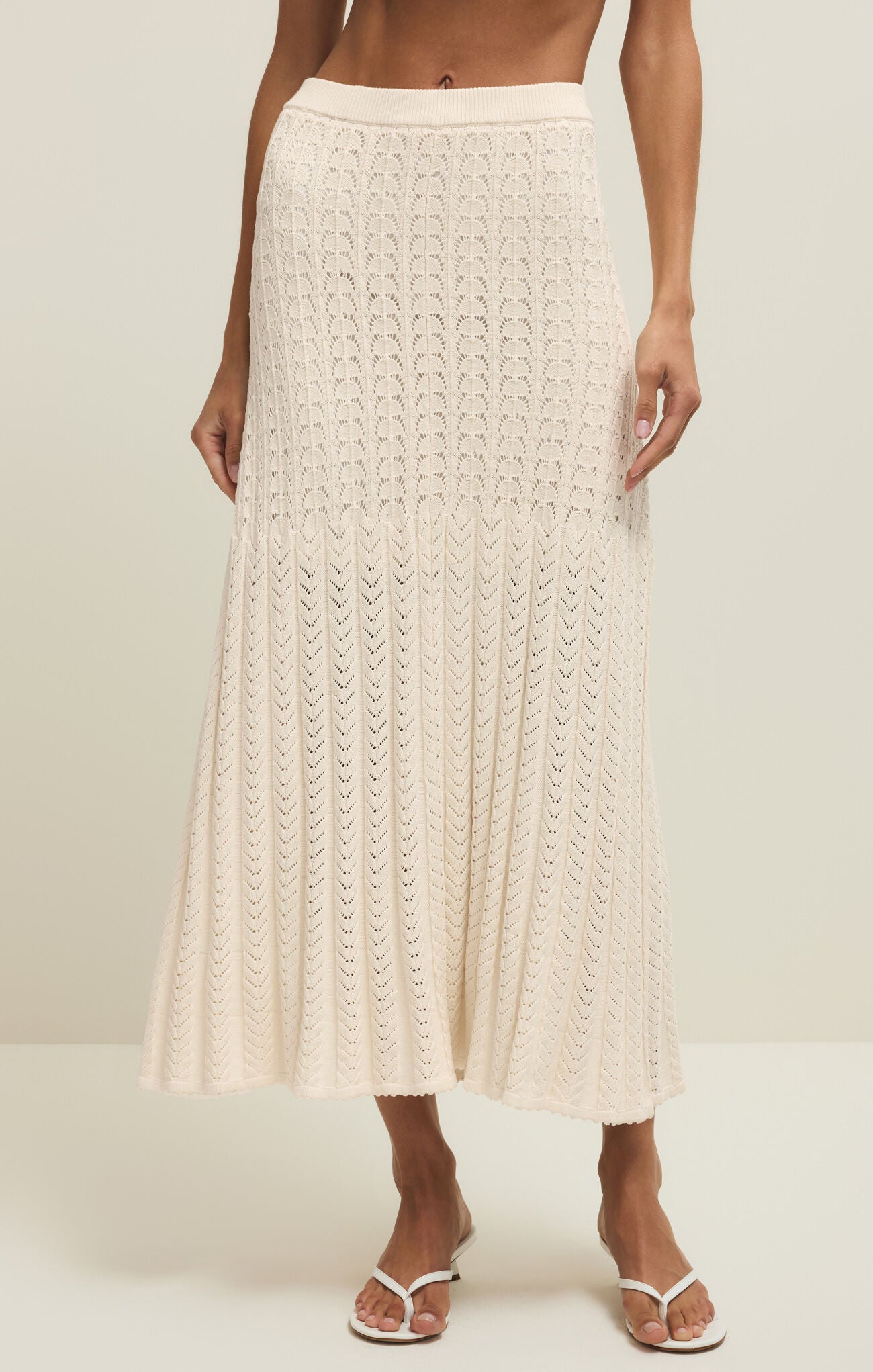 Person wearing a beige crochet skirt on a plain background