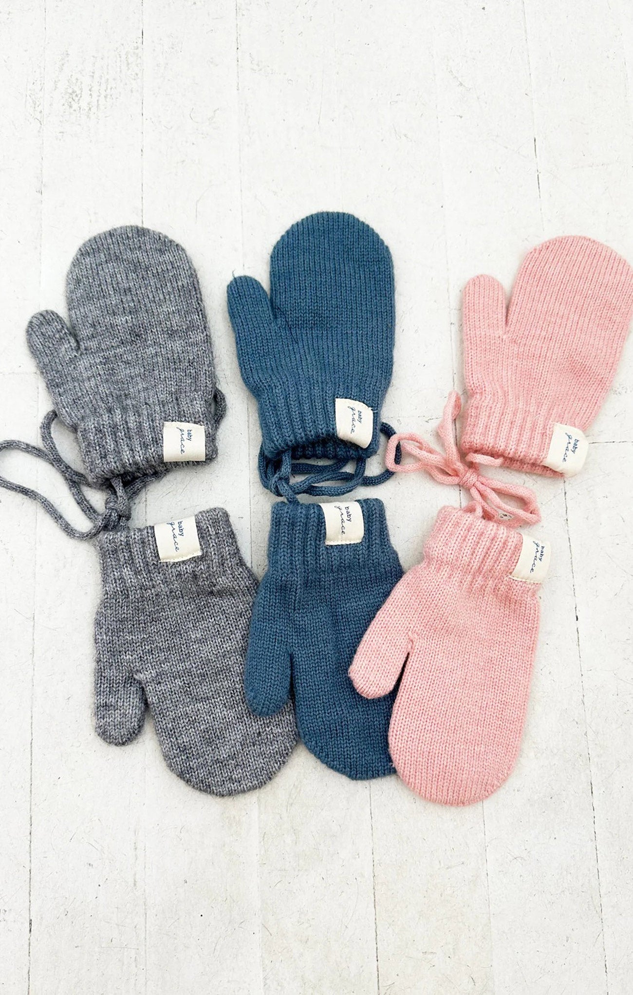 Set of six pairs of knitted mittens in gray, blue, and pink on a light wooden surface.