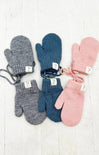 Set of six pairs of knitted mittens in gray, blue, and pink on a light wooden surface.
