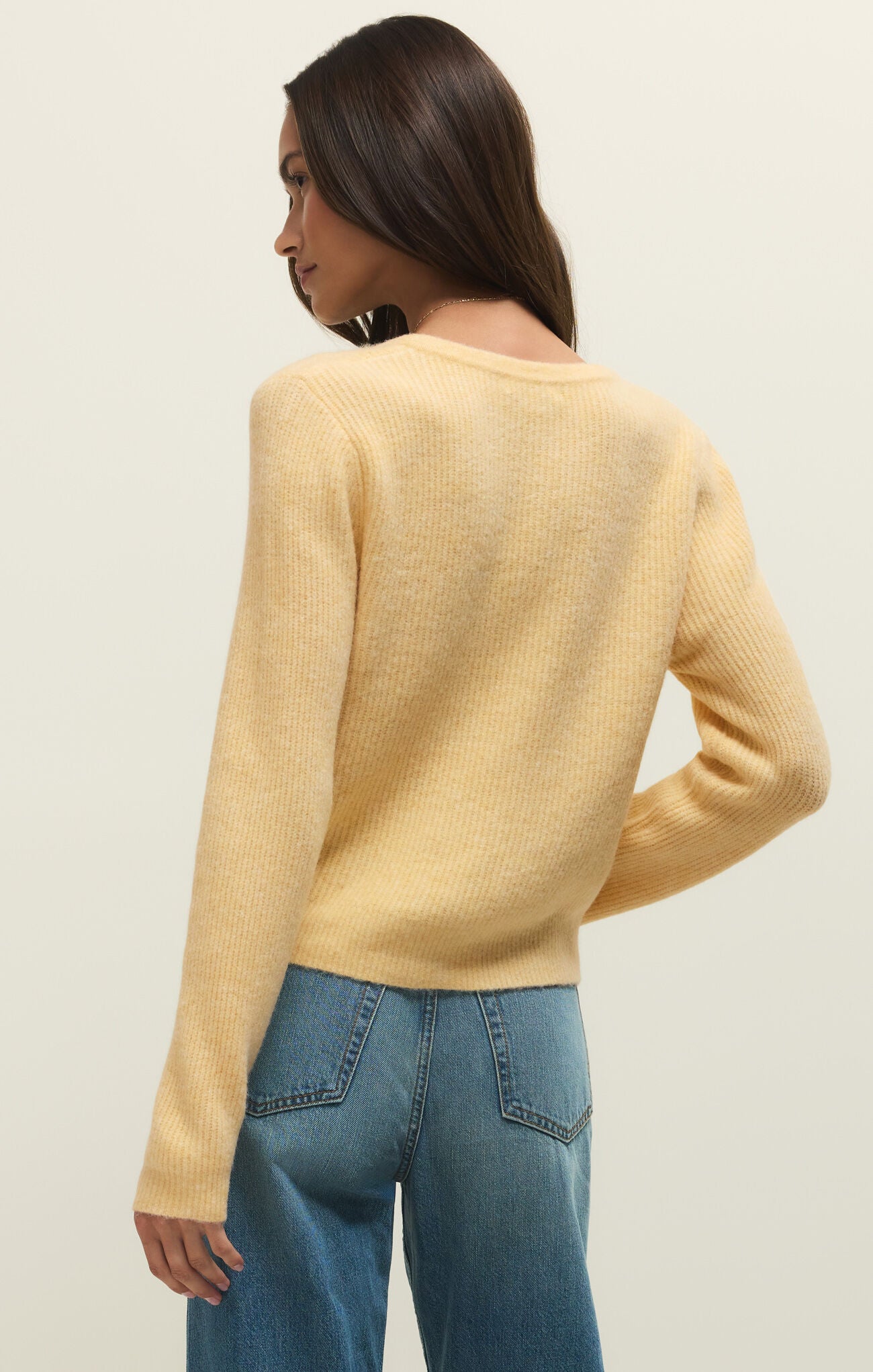 Person wearing a yellow sweater and blue jeans on a plain background